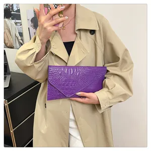 Detail of a purple crocodile pattern envelope clutch bag held against a khaki trench coat
