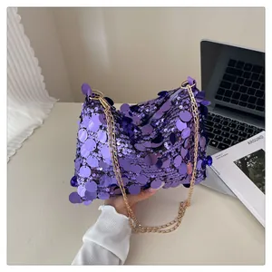Dettaglio borsa con paillettes viola e catena dorata su sfondo scrivania minimalista