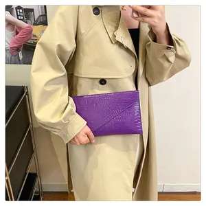 Detail view of purple crocodile texture envelope clutch held by a model with a beige coat