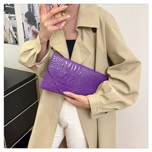 Detail of purple envelope clutch with faux crocodile texture held by a fashion model