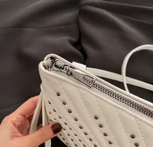 Detail of silver smooth metal zipper closure on white quilted handbag with studs