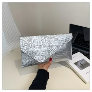 Detail shot of a silver envelope clutch with crocodile embossing held in hand