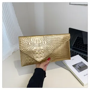 Detail of a luxury gold crocodile embossed envelope clutch bag held by a model