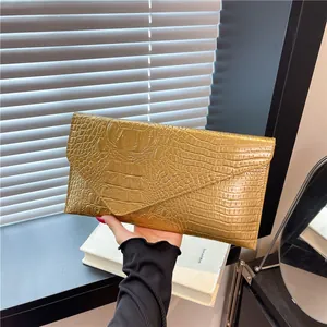 Elegant gold crocodile embossed envelope clutch bag held against a minimal background