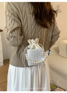 Dettaglio borsa a secchiello bianca con trama a scaglie e manico di perle indossata con maglione