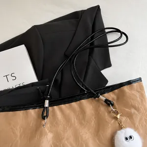 Detalle del bolso tote marrón arrugado con asas negras delgadas y colgante de felpa blanco