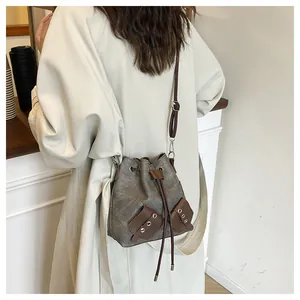 Détail du sac seau en toile grise avec garniture en cuir marron et cordon sur modèle