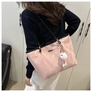 Detail of pink tote bag with crinkled texture, black straps and a white fuzzy charm
