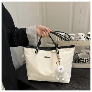 Close-up of a large beige tote bag with black trim and a cute plush doll charm