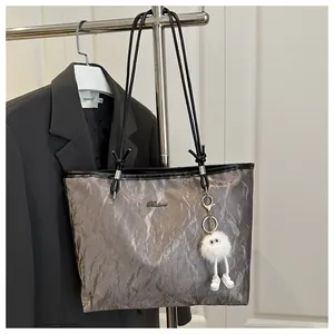 Detail of grey textured tote bag with metal logo and white plush doll charm