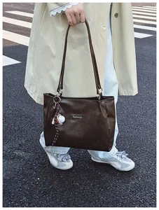 Detail of dark brown leather tote bag featuring a baseball charm and street fashion style