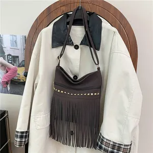 Sac bandoulière marron en daim avec franges et rivets dorés sur un trench-coat beige