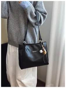 Detail of black leather tote bag with fashion logo and baseball pendant decoration