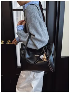 Detail of black PU leather tote with fashion logo patch and sports-themed keychain