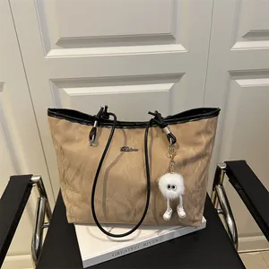 Large khaki tote bag with black handles and cute plush charm on a luxury chair