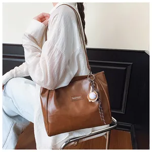 Detail of a large brown tote bag with textured leather and a baseball shaped pendant charm