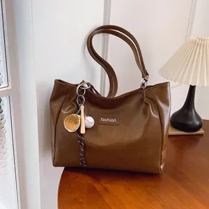Large brown leather tote bag with fashion tag and baseball charm on a wooden table