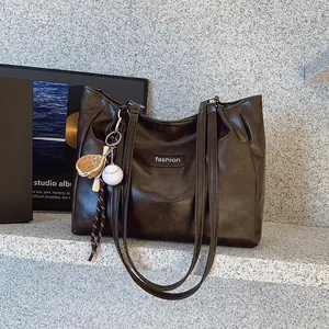 Deep brown leather tote bag with fashion tag and baseball charm on a studio steps background