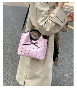 Détail du sac à bandoulière rose avec broderie noire et nœud sur un trench-coat beige