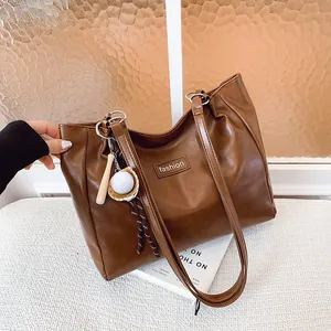 Large brown leather tote bag with fashion tag and baseball charm on a white surface