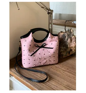 Détail du sac matelassé rose avec imprimés nœuds et ruban noir sur une table en bois