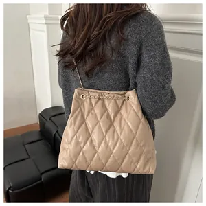 Detail of beige quilted bucket bag with gold chain strap worn by a model in casual setting