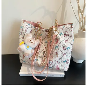 Detail of white textured tote bag with pink cartoon motifs and golden chain strap