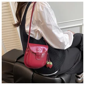 Detailansicht der roten PU-Satteltasche mit Erdbeeranhängern auf weißem Outfit