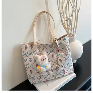 Close-up of white tote bag featuring pink cartoon prints and a plush bear charm