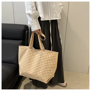 Detail of a large yellow and white gingham canvas tote bag held by a model