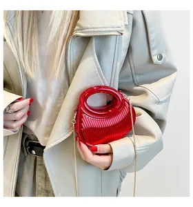 Détail de la pochette plissée rouge métallisé avec chaîne dorée sur manteau ivoire