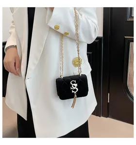 Détail du sac bandoulière en velours noir matelassé avec pompon doré sur un blazer blanc