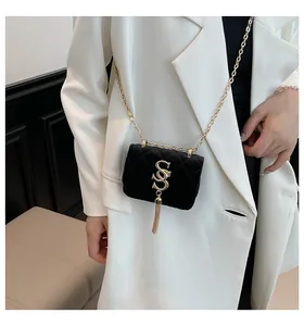 Détail du mini sac matelassé en velours noir avec logo S doré et gland sur blazer blanc