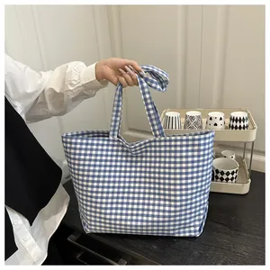 Detail of blue and white checkered canvas tote bag with long shoulder straps in a home setting