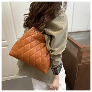 Detail of orange-brown quilted tote bag with metal chain strap worn by a model