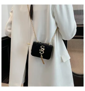 Détail du sac carré en velours noir avec chaîne dorée et pompon sur un manteau blanc