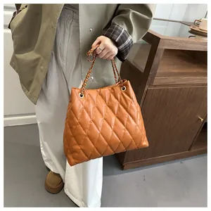 Detail of orange quilted tote bag with interwoven metal chain strap and PU leather texture