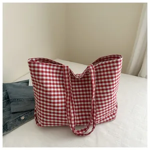 Detail of red and white gingham canvas tote bag laid on white bedding with denim jacket