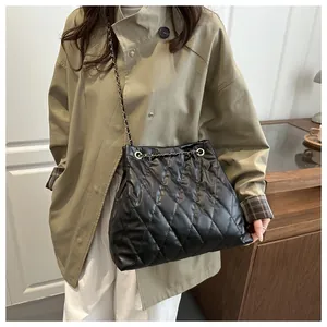 Close-up of black quilted leather bucket bag with chain strap worn by a model