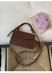 Detail of a brown woven crossbody bag featuring a twisted handle and V-pattern texture