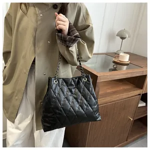 Close-up of black quilted tote bag with gold chain strap on professional trench coat