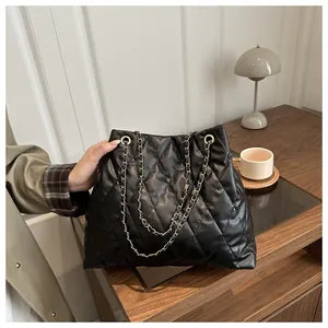 Detail of black quilted leather tote bag featuring elegant gold metal chain straps