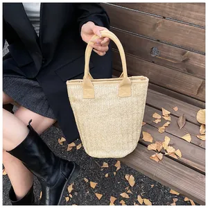 Close-up of woven straw bucket bag on wooden bench with yellow leaves in autumn sun