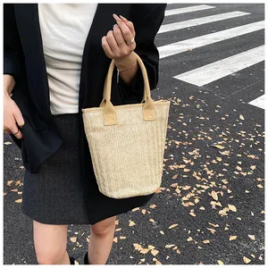Detail of beige straw bucket bag with herringbone weave and reinforced handles on urban street