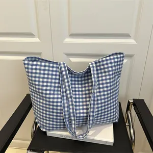 Casual blue and white gingham canvas tote bag with wide straps on a white door background