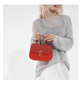 Détail d'un sac à main rouge pailleté avec boucle dorée porté par un mannequin en tricot