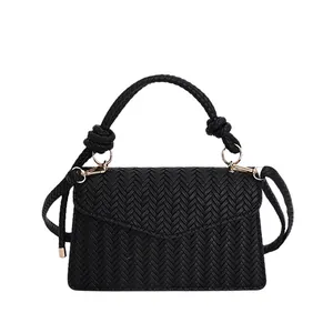 Minimalist black woven faux leather handbag with triangular flap and gold hardware details
