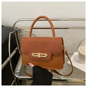 Detail view of caramel brown handbag featuring textured flap and gold metal bar lock
