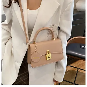 Dettaglio borsa a tracolla beige con chiusura a scatto dorata e ciondolo alla moda