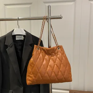 Quilted caramel tote bag with gold chain strap shown in a modern urban style setting